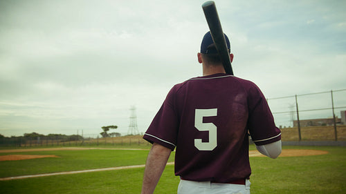 Baseball player walking on field with bat and glove