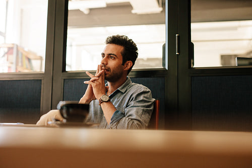 Thoughtful young man sitting at table in conference room