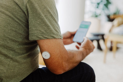 Senior checks glucose monitor on smartphone at home