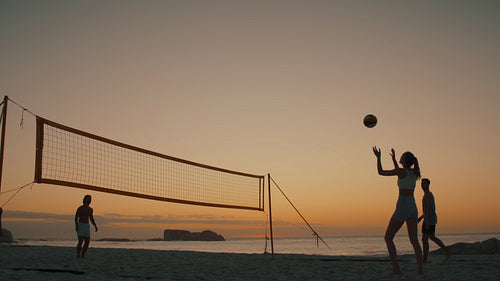 Static wide shot of skilled friends playing beach volleyball as the sun goes down