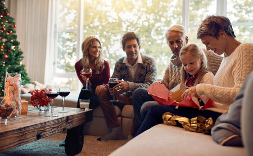Cute girl with family and opening christmas present