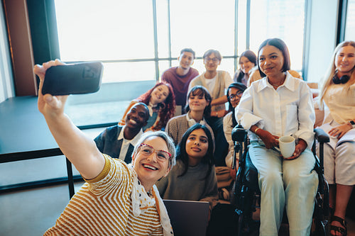 Happy teacher taking a selfie with diverse class of smiling students in a bright classroom setting