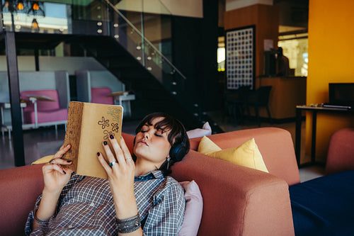 Young female college student reading while relaxing on a comfortable couch in a modern lounge area