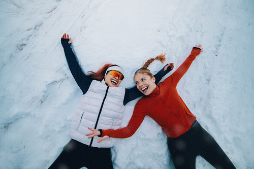 Together, female runners make snow angels in fresh winter snow after a run