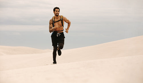 Healthy young man running over sand dunes