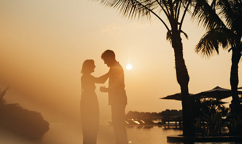 Romantic couple on vacation enjoying sunset at exotic hotel with palm trees