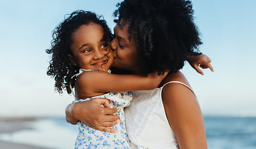 Loving mother hugging daughter on beach, sharing happiness and love