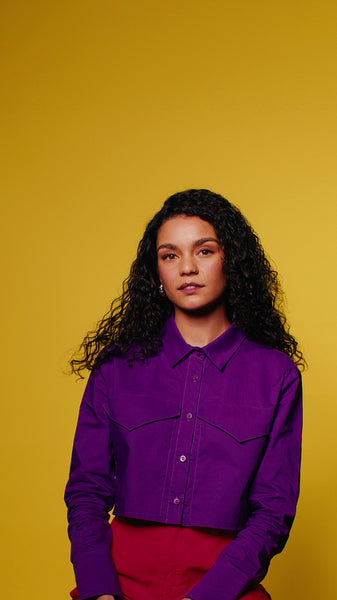 Young woman smiles confidently in purple shirt against yellow background
