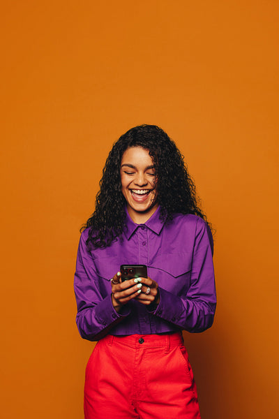 A vibrant woman texting on a orange background, using a smartphone