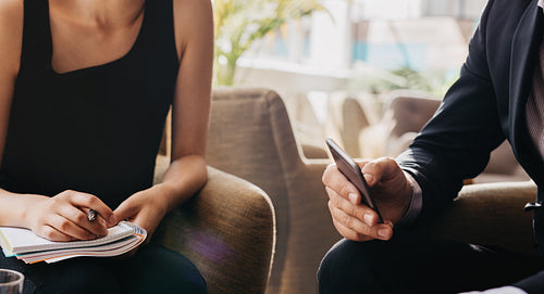 Businessman holding mobile phone and woman with notepad