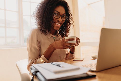 Businesswoman enjoying a cup of coffee while working on laptop at home