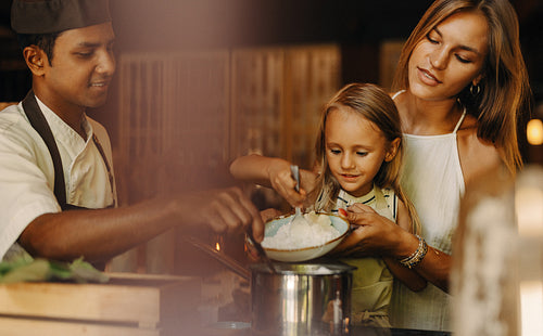 Chef teaching mother and child cooking skills in a restaurant kitchen setting