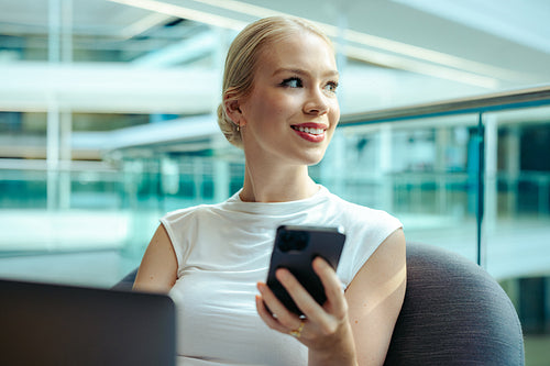 Confident female accountant looking at phone in modern office
