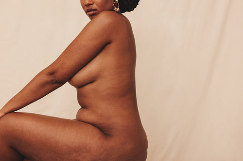 Confident young woman sitting naked in a studio