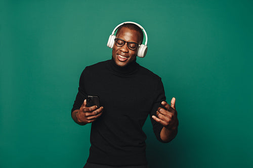 Smiling young man enjoying trendy music playlist on smartphone with wireless headphones