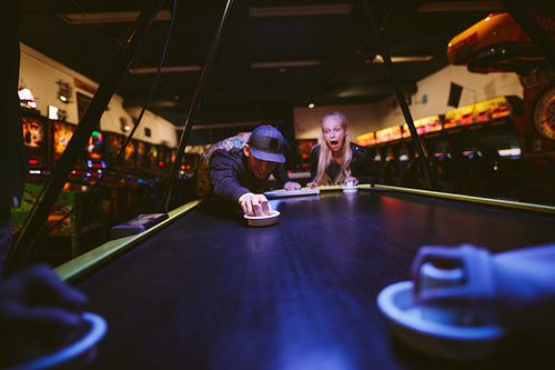 Happy young friends playing air hockey at amusement park