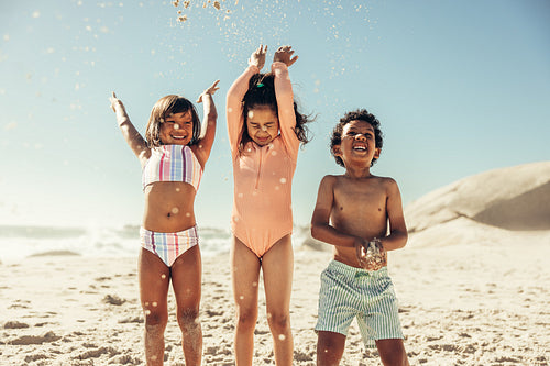 Happy kids throwing beach sand into the air