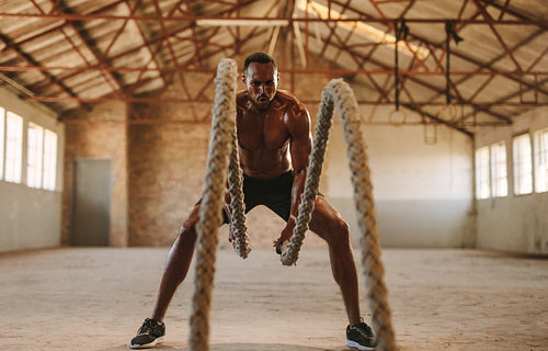 Muscular man working out with battle ropes
