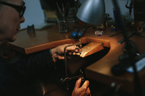 Female jewelry maker cutting metal with a band saw