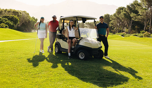 Group of golfers posing with golf cart and clubs on a sunny day, showcasing teamwork on the lush green course