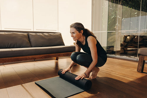 Happy senior woman rolling up a yoga mat at home
