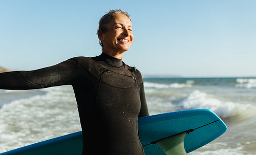 Mature woman smiling on the beach holding a surfboard