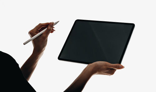 Hands holding a tablet with a stylus against a plain background