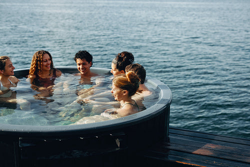 Adults relax in outdoor hot tub spa by the water for wellness and leisure