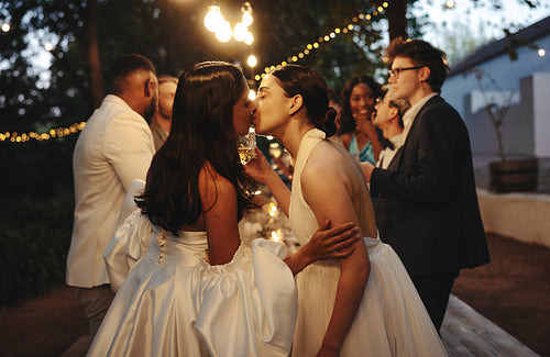Two brides kissing during outdoor LGBTQ wedding party