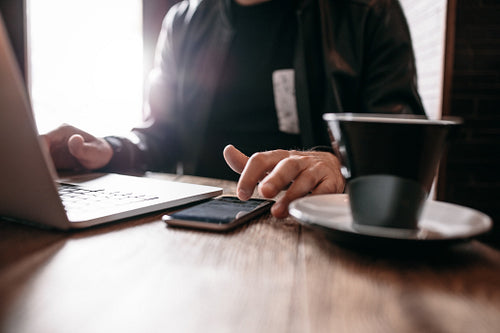 Man at cafe with laptop using mobile phone