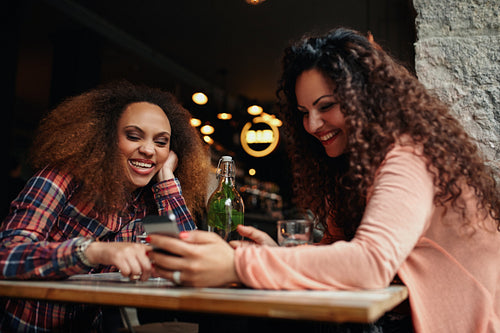Women having fun using a smart phone in cafe