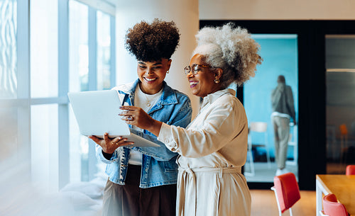 Two women collaborate on laptop in modern office