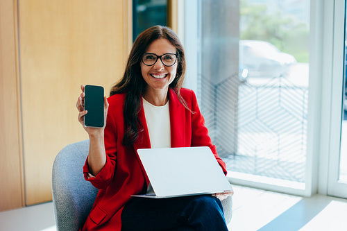 Professional woman holding a smartphone and laptop in an office environment