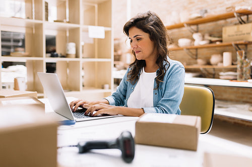 Cheerful online store owner using a laptop in a warehouse