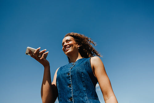 Young woman speaks on smartphone under a clear blue sky outdoors