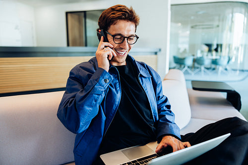 Man on the phone, smiling and working on laptop in office