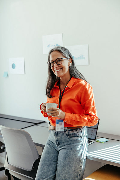 Confident woman in office holding coffee mug and smiling during a work break