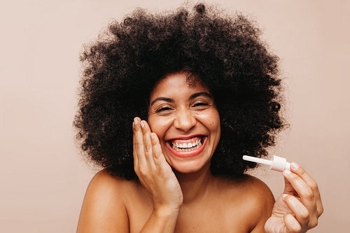 Happy woman with Afro hair applying beauty oil on her face