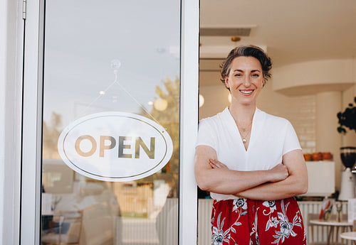 Successful cafe owner smiling while standing at the doorway of her newly opened restaurant