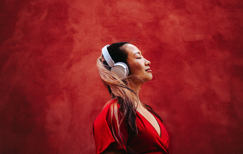 Woman enjoys music with headphones in red studio portrait