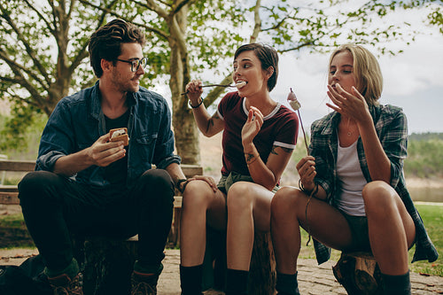 Friends eating toasted marshmallows sitting outdoors