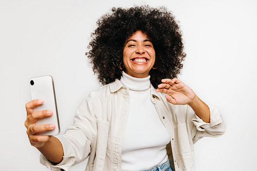 Gorgeous woman with curly hair taking a selfie in a studio
