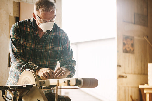 Senior carpenter with mask using belt sander