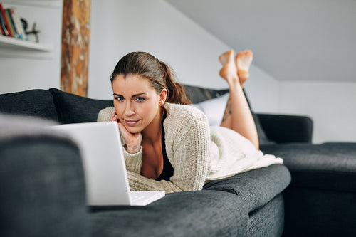 Pretty young female lying on sofa with a laptop