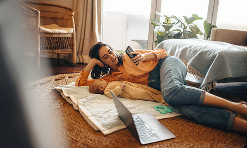 Mother relaxing on floor with baby while video calling at home