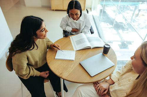 College students studying together at a table with books and laptops in an academic setting