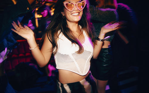 Excited young woman dancing at a party wearing heart-shaped sunglasses