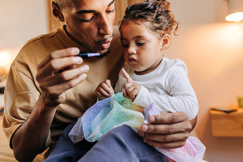 Dad painting his daughter's nails with nail polish at home