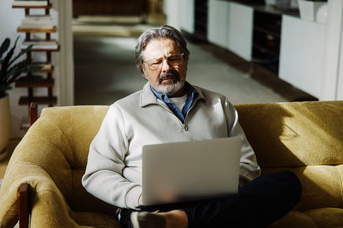 Gray-haired senior man types on a laptop at home