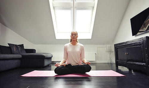 Young woman meditating in lotus position at home